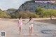 A couple of women walking down a dirt road holding hands.