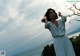 A woman in a white dress standing on a cliff overlooking the ocean.