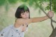 A woman in a white dress leaning against a tree.