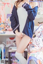 A woman in a white top and blue jacket posing on a bed.